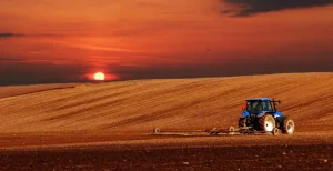 A well-maintained blue farm tractor operating at sunset, demonstrating extended machinery lifespan through regular maintenance.