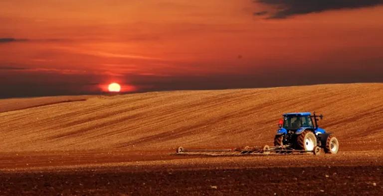 A well-maintained blue farm tractor operating at sunset, demonstrating extended machinery lifespan through regular maintenance.